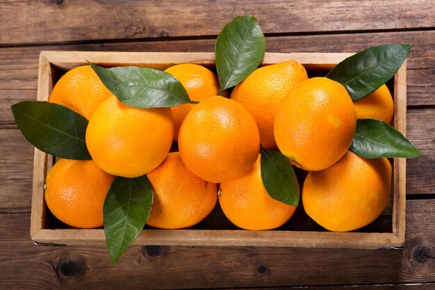 Vers oranje fruit met bladeren in een doos op houten tafel, bovenaanzicht