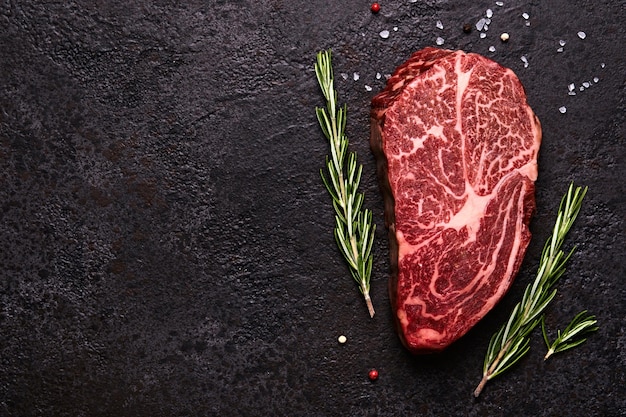 Vers rauw gemarmerd rundvlees rib eye steak en kruiden op zwarte stenen achtergrond kopie ruimte