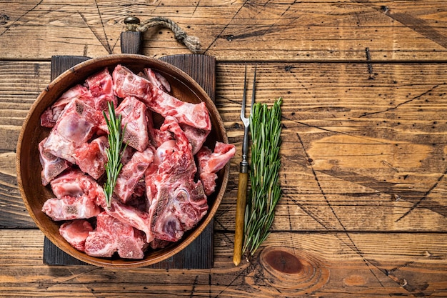 Vers rauw vlees op het bot in blokjes gesneden voor goulash in een houten bord. Houten achtergrond. Bovenaanzicht. Ruimte kopiëren.