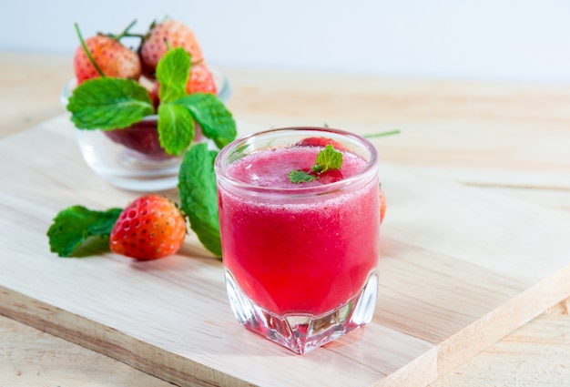 Vers rood aardbeien sap in transparant glas voor drank op hout