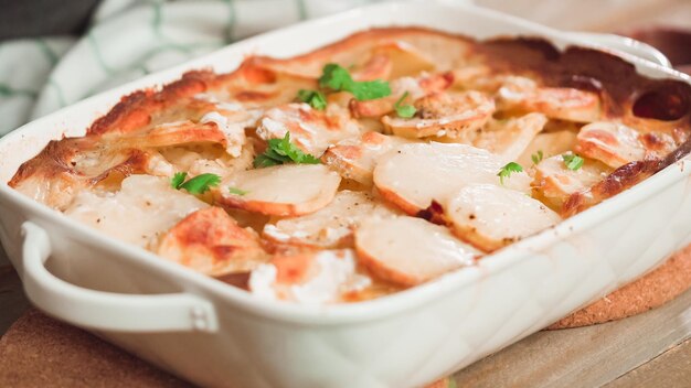 Vers uit de oven gebakken geschulpte aardappelen garneer met peterselie in een witte keramische ovenschaal.