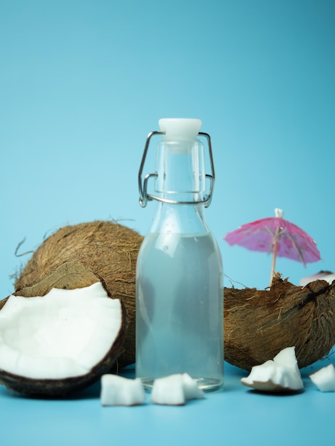 Vers verfrissend kokoswater in een fles met een open kokosnoot met wit vruchtvlees op een blauwe geïsoleerde blauwe achtergrond