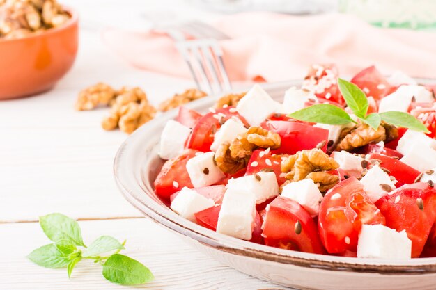 Vers voorgerecht van tomaten, fetakaas, walnoten, lijnzaad en sesamzaadjes in een bord op een witte houten tafel