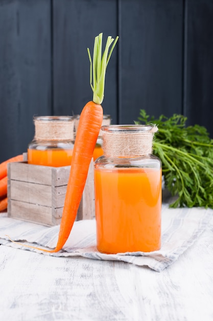 Vers wortelsap in een kruik. verse wortelen met bladeren en drinken. lente voedsel voor gezondheid en schoonheid