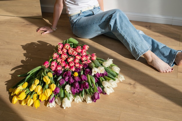 Verscheiden kleurrijke tulpen op de vloer met een vrouw die in natuurlijk licht zit