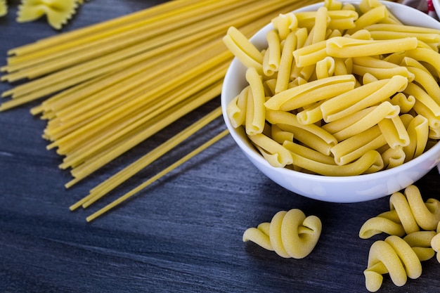 Verscheidenheid aan biologische droge pasta op een houten bord.