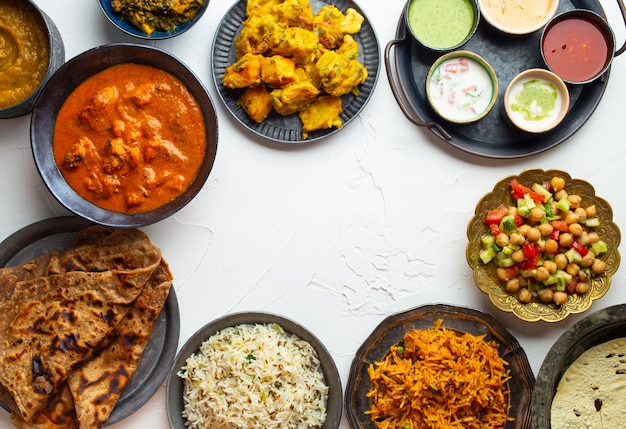 Verscheidenheid aan Indiaas eten, verschillende gerechten en snacks op witte rustieke achtergrond. Pilaf, butter chicken curry, rijst, palak paneer, chicken tikka, dal soup, naan bread, assortiment chutney. Bovenaanzicht