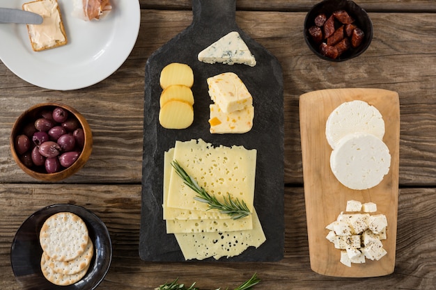 Verscheidenheid van kaas, olijven, koekjes en rozemarijn kruiden op houten tafel