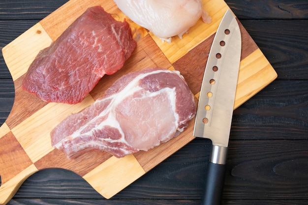 Verscheidenheid van rauw vlees rundvlees op been, varkensvlees en kipfilet op houten tafel met slager mes, bovenaanzicht