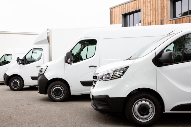 Verschillende auto's bestelwagens vrachtwagens geparkeerd op parkeerplaats te huur levering witte bestelwagens in dienst bestelwagen vrachtwagen voorkant van ingang van magazijn distributie logistieke samenleving