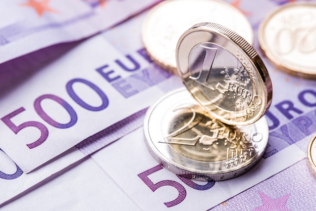 Verschillende bankbiljetten en munten van 500 euro liggen naast elkaar. symbolische foto voor wealt.euro munt balanceren op stapel met achtergrond van bankbiljetten.