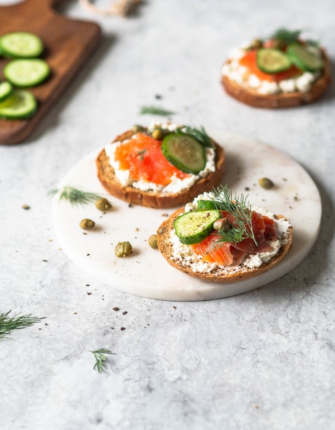 Verschillende broodjes op roggebrood met roomkaas, zalm, verse komkommer en kruiden.