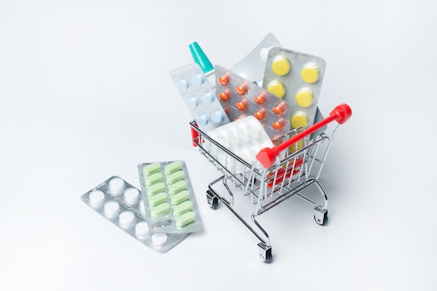 Verschillende capsules, tabletten en medicijnen in winkel trolley op een blauwe ondergrond