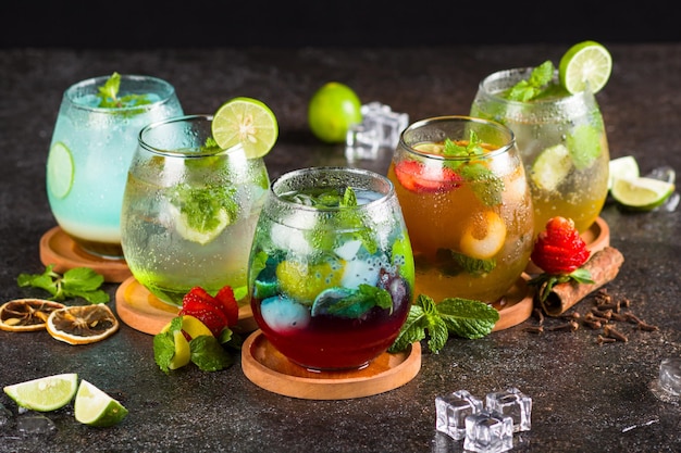 Verschillende cocktails in glas met ijsblokjes, aardbei, limoen, gember en muntblad op textuurtafel