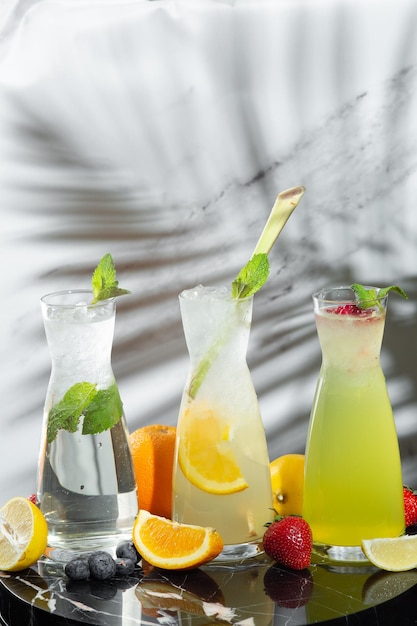 Verschillende drankjes in glazen kannen op tafel en schaduw van tropische plant op lichte achtergrond. Verschillende drankjes in glazen kannen met kopieerruimte.