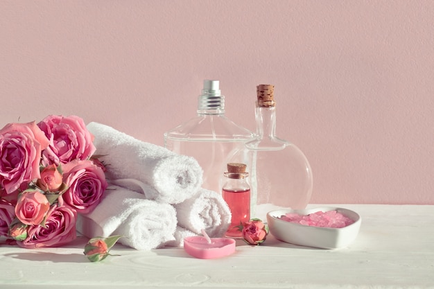 Verschillende flessen cosmetica en katoenen handdoeken op een roze oppervlak met rozen