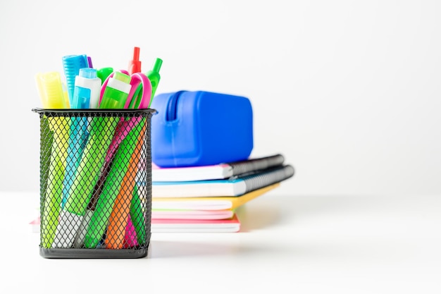 Verschillende gekleurde stiften en pennen in een potloodhouder naast enkele boeken en een etui op een wit