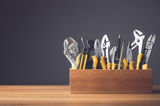 Verschillende gele gereedschapskit voor doe-het-zelf in houten kist op houten bureau met grijze muur