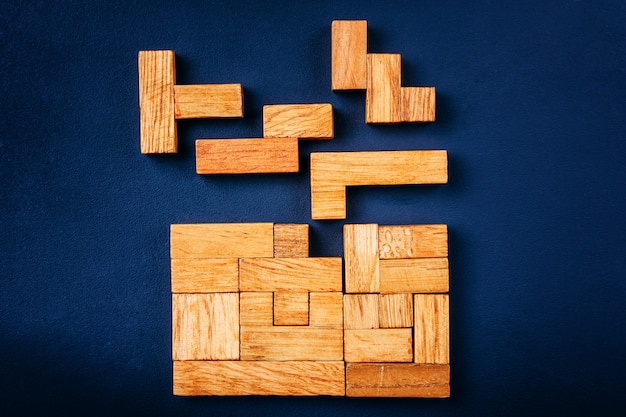 Verschillende geometrische vormen houten blokken schikken in solide figuur op een donkere achtergrond.