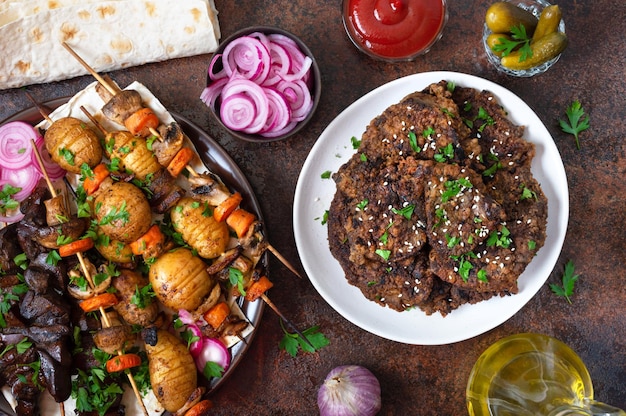 Verschillende gerechten van leverkebab aan spiesjes spiesjes met hele levergroenten en champignons