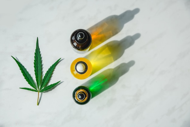 Verschillende glazen flessen met cbd-olie, thc-tinctuur en cannabisbladeren op gele achtergrond plat gelegd