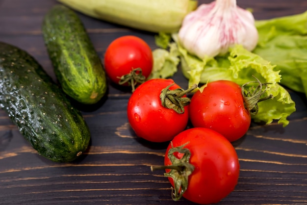 Verschillende groenten op houten planken. Tomaten, komkommers, sla en courgette op een donkere tafel. Detailopname.