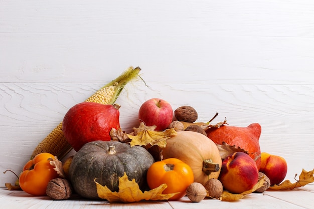 Verschillende groenten, pompoenen, appels, peren, noten, maïs, tomaten en droge bladeren op witte houten achtergrond. Herfstoogst, copyspace.