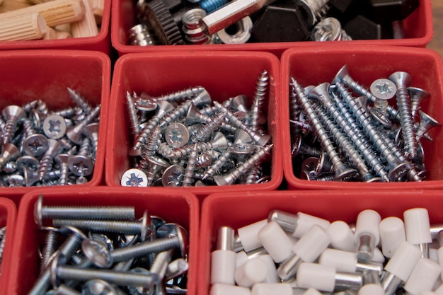 Verschillende grootte en vorm van schroeven, bouten, houten pinnen, selectie in rode plastic bakdoos op een houten achtergrond Montageset voor meubels Selectieve focus