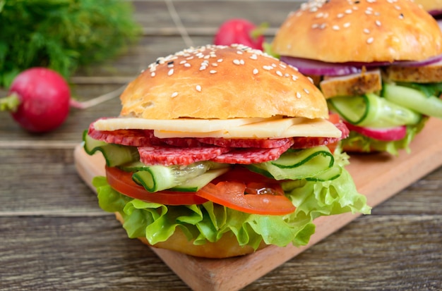 Verschillende hamburgers op een houten bord. Zelfgemaakt broodje met ham of vlees of salami, groenten, kruiden. Broodjes voor de lunch.