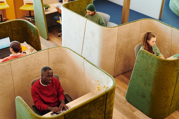 Foto verschillende jonge interculturele collega's in vrijetijdskleding zitten aan bureaus op kantoor en kijken naar laptopschermen tijdens individueel werk