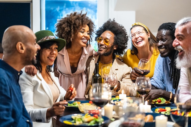 Verschillende mensen van leeftijd en etniciteit eten een veganistisch diner. Multi-etnische groep vrienden die plezier hebben tijdens het delen van een maaltijd in een warm en gastvrij huis.