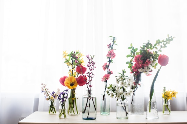 Verschillende mooie bloemen in potten met water op de tafel bij het raam