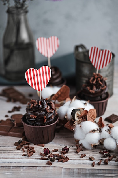 Verschillende muffins of cupcakes met chocoladevormige room aan witte tafel. een kerstkaart in de vorm van een hart voor valentijnsdag in een van hen.