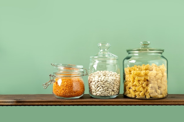 Verschillende peulvruchten in glazen potten: pasta, bonen, linzen op groene achtergrond. Geen afvalopslag, plasticvrij.