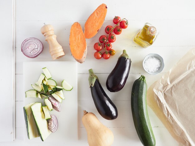 Verschillende rauwe groenten zoete aardappel, cherrytomaatjes, aubergine en pompoen klaar om te bakken op een zelfgemaakt veganistisch recept