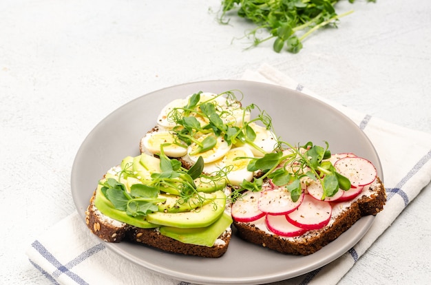 Foto verschillende sandwiches met radijs, avacado, ei en microgreens op een grijze plaat op een lichte achtergrond. plat leggen, gezonde snack. detailopname.