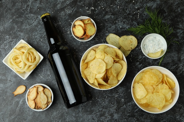 Verschillende snacks en flesje bier op zwarte smokey oppervlak