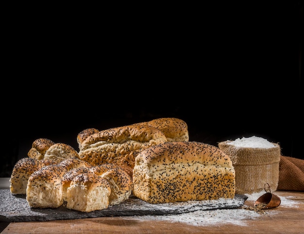 Verschillende soorten brood gemaakt met sesamzaadjes (gergelim) op rustieke houten tafel met andere soorten brood en ingrediënten op de achtergrond.