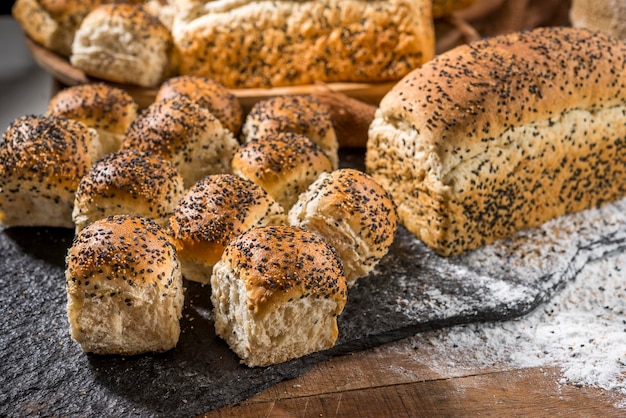 Verschillende soorten brood gemaakt met sesamzaadjes (gergelim) op rustieke houten tafel met andere soorten brood en ingrediënten op de achtergrond.