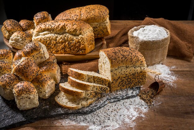 Verschillende soorten brood, gesneden, gemaakt met sesamzaadjes (gergelim) op rustieke houten tafel met andere soorten brood en ingrediënten op de achtergrond.