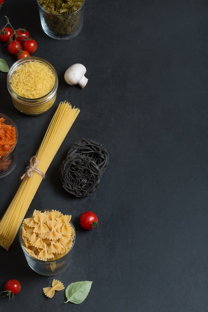 Verschillende soorten Italiaanse pasta met groenten op het donkere bord