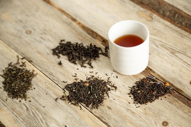 Verschillende soorten natuurlijke thee op een lepel en gebrouwen in een glas op een houten achtergrond.