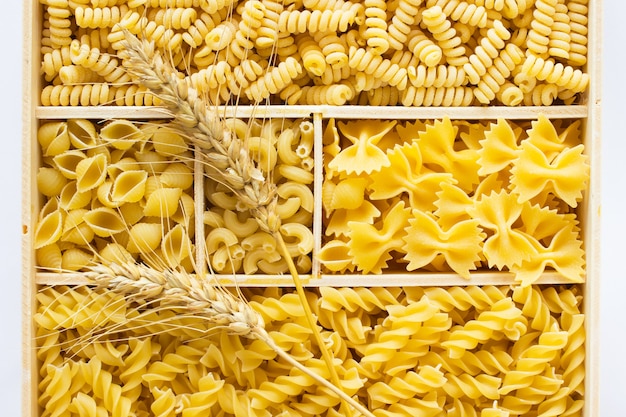 Verschillende soorten pasta in een houten kist. Twee takjes tarwe