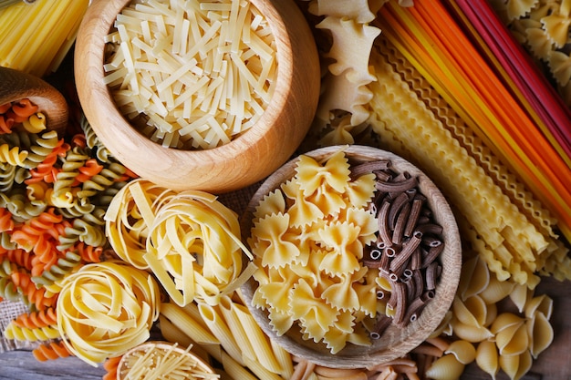 Verschillende soorten pasta met houten kommen op tafel, macroweergave