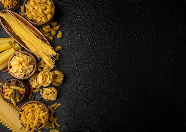 Verschillende soorten pasta op zwarte achtergrond met kopieerruimte, bovenaanzicht