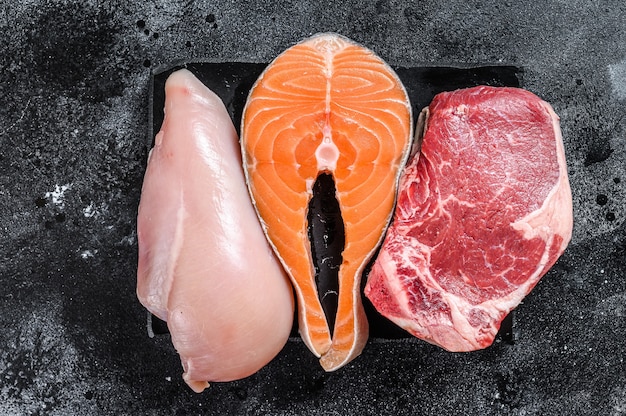 Verschillende soorten rauw vlees steaks Runderlende, zalm en kipfilet. Zwarte achtergrond. Bovenaanzicht.