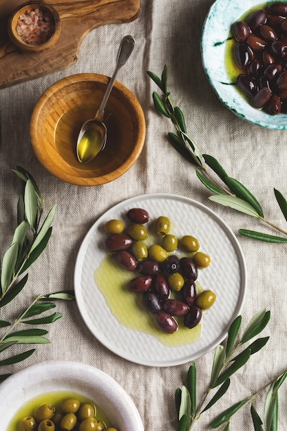 Foto verschillende soorten verse olijven in verschillende keramische platen op een oude vintage grijze tafelkleedtafel. natuurlijk productconcept. rustiek vintage bestek.