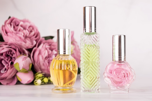 Verschillende transparante parfumflesjes met boeket van pioenrozen op lichte marmeren achtergrond