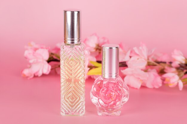 Verschillende transparante parfumflesjes met lente bloeiende boomtak op roze achtergrond. Aromatische essentieflessen