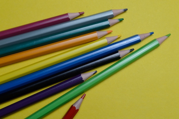 Verschillende veelkleurige potloden liggen op het gele oppervlak.